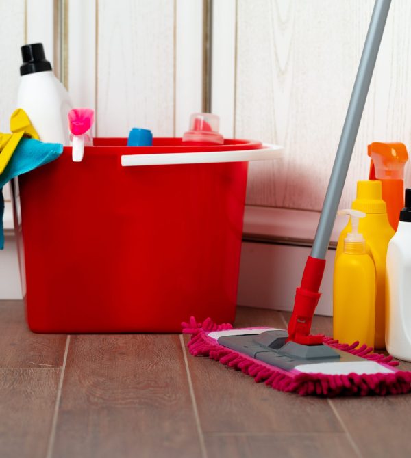 Various household cleaning detergents and bottles in a plastic bucket on the floor. Housekeeping concept